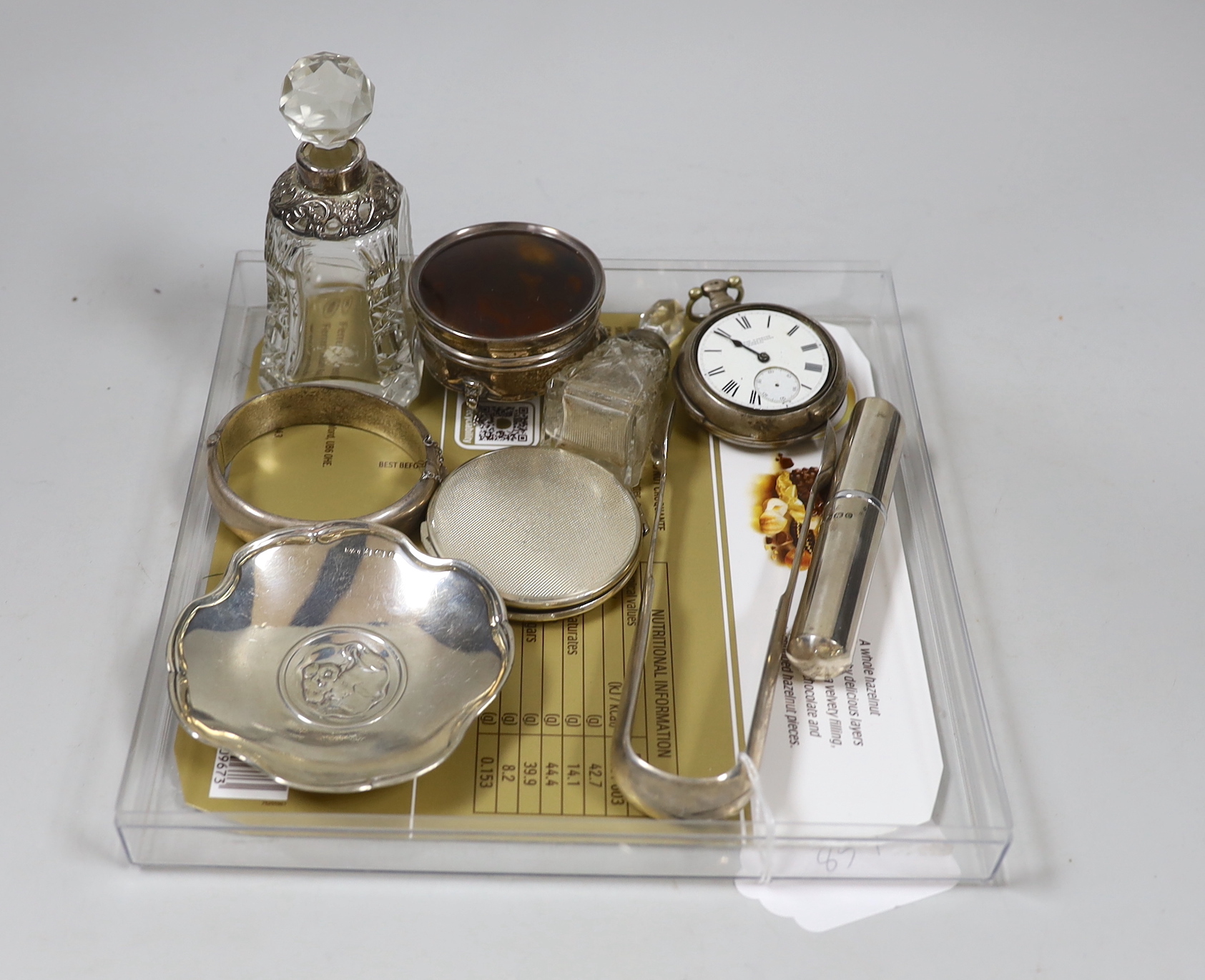 Sundry silver including a George V tortoiseshell mounted trinket box, diameter 6cm, two mounted glass scent bottles, modern atomiser, tongs, dish, compact, bangle and a verge pocket watch.
